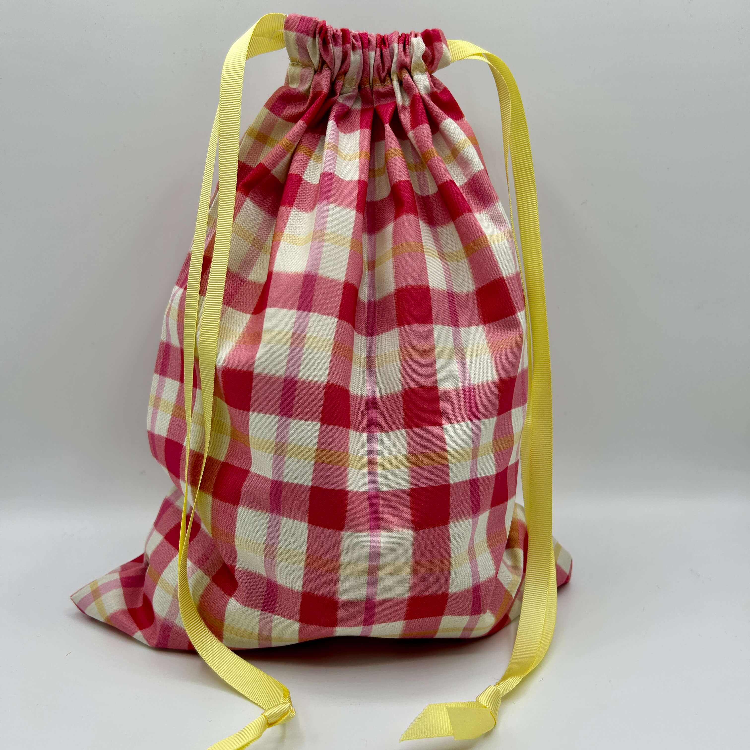 Red and white checkered drawstring bag with yellow straps on a light gray background