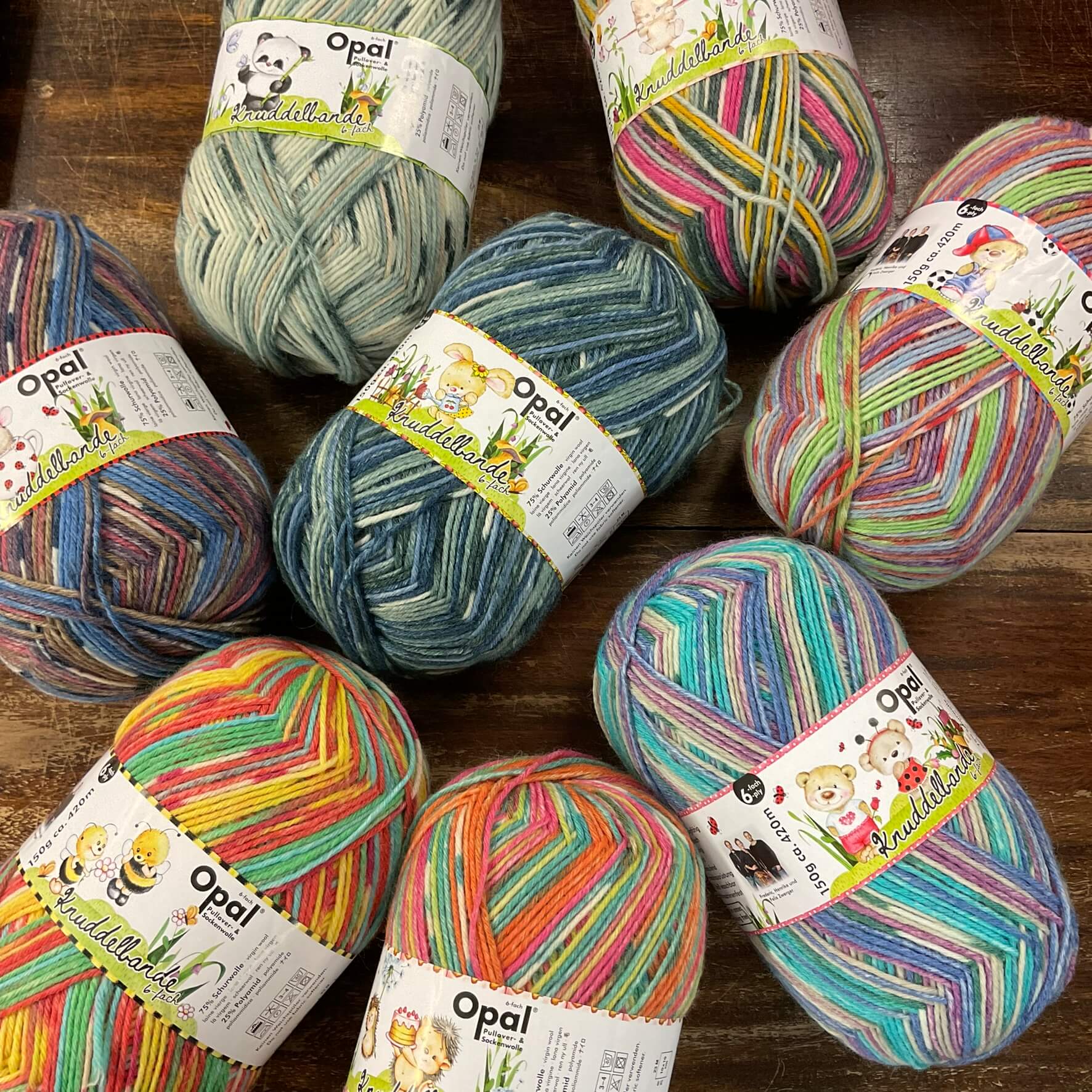 8 balls of multicoloured opal 6ply sock wool yarn on a wooden table at The Woolly Brew yarn shop